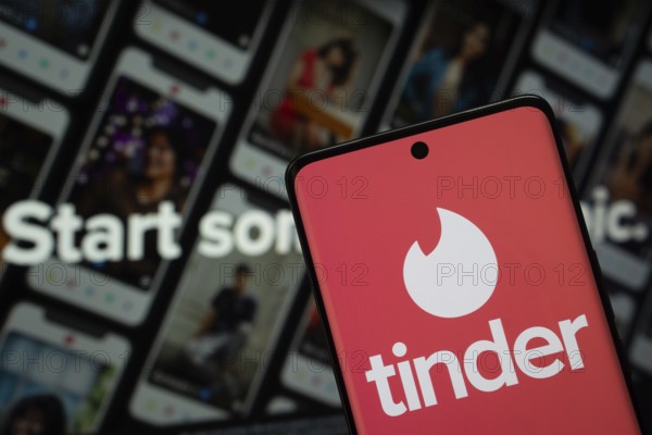 Dhaka, Bangladesh - 18 March 2025: The logo of the tinder is displayed on a smartphone screen, and the website tinder is visible on a computer screen in the background