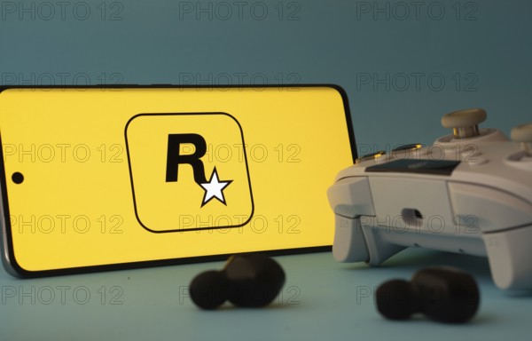 Dhaka, Bangladesh- 17 June 2025: A smartphone with a rockstar games app icon next to a controller and earbuds on a blue surface