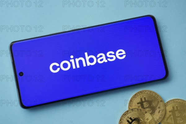 Dhaka, Bangladesh- 17 June 2025: Smartphone displaying Coinbase logo with Bitcoin coins on a blue background