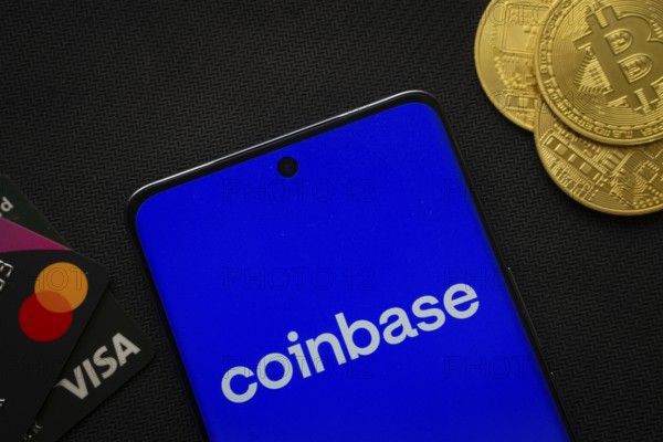 Dhaka, Bangladesh- 17 June 2025: Smartphone displaying Coinbase logo surrounded by Bitcoin coins and payment cards