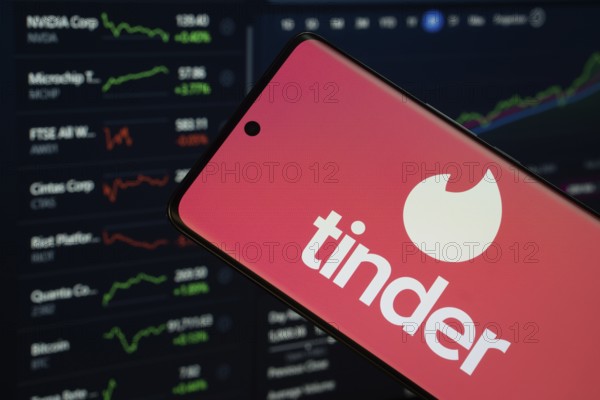 Dhaka, Bangladesh- 18 March 2025: tinder logo is displayed on a smartphone screen, with a stock graph webpage visible on a computer screen in the background