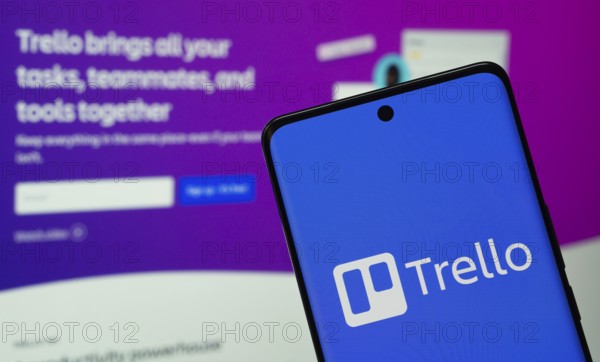 Dhaka, Bangladesh - 18 March 2025: The logo of the trello is displayed on a smartphone screen, and the website trello is visible on a computer screen in the background