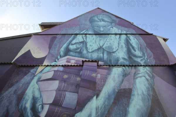 Mural Knowledge by Sokar Uno 2023, blue violet house wall, woman carrying a stack of books, books, reading, learning, view from below, street art, graffiti, double image, Weißenfels, Saxony-Anhalt, Germany