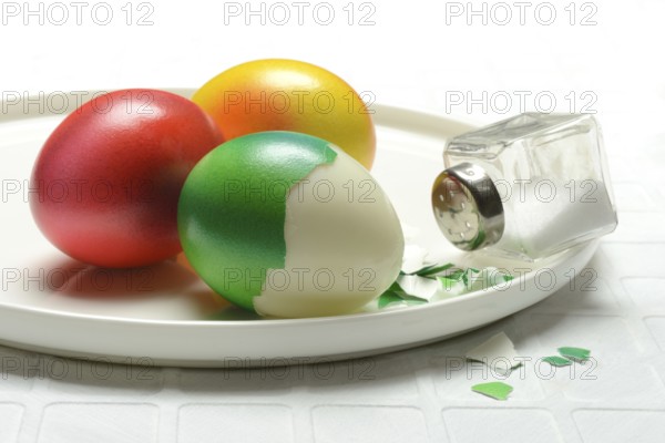 Easter eggs and salt shaker on plate, partially peeled