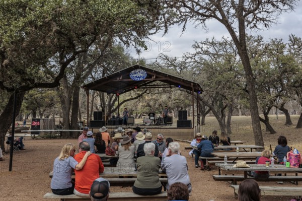 Tourists drinking beer at an open-air bar with a bandstand in Luckenbach, Texas, USA