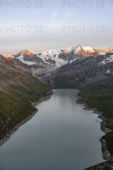 View at the summit of Mont de la Blana, alpenglow at sunset, view of a blue mountain lake, Lac des Dix reservoir, behind mountain peak Mont Blanc de Cheilon with glacier, Hérménence, Valais Alps, Valais, Switzerland