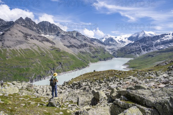Mountaineer on a hiking trail at a blue mountain lake, reservoir Lac des Dix, behind mountain peak Mont Blanc de Cheilon, Hérménence, Valais Alps, Valais, Switzerland