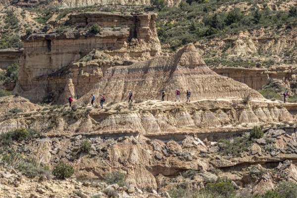 Group of hikers at colorful sandstone rock formations, desert, along gravel road Ruta Jubierre, Desierto de los Monegros, Spain