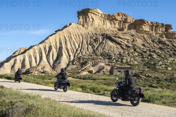 Biker riding motorcycle, gravel road, colorful rock formation, semi-desert, Bardena Blanca area, Bardenas Reales Nature Park, Navarre, Spain