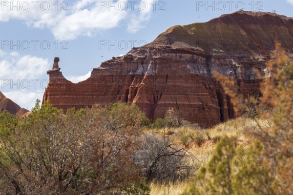 The Lighthouse rock hoodoo behind a field of grass and shrubs at Palo Duro Canyon State Park near Amarillo, Texas