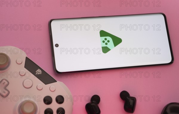 Smartphone with Google Play Games logo, game controller, and earbuds on a pink background