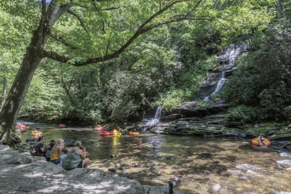 Visitors swimming and floating on inflatables at the base of Tom Branch Falls along Deep Creek in the Smoky Mountains near Bryson City, North Carolina, USA