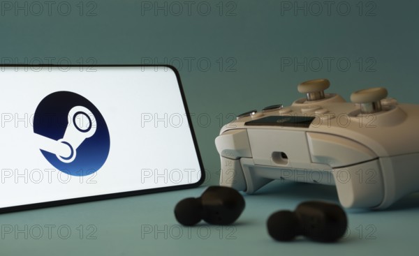 A smartphone with a Steam app icon next to a controller and earbuds on a blue surface