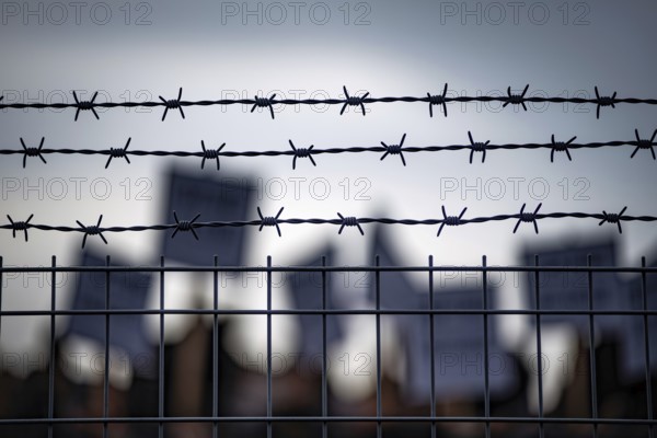 Barbed wire fence with blurred protesters and signs in background during border or prison demonstration Generative AI, AI generated