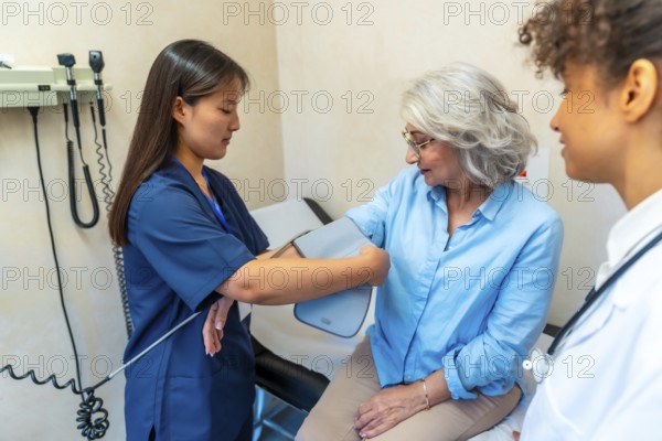 Nurse using sphygmomanometer, taking blood pressure of elderly woman during medical consultation in hospital or private clinic