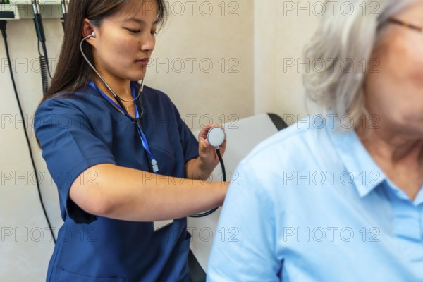 Female doctor using stethoscope examining lungs of senior patient during medical checkup in hospital room