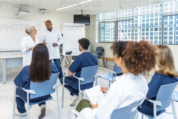Doctors and nurses listening to senior colleagues giving presentation during medical conference in hospital meeting room