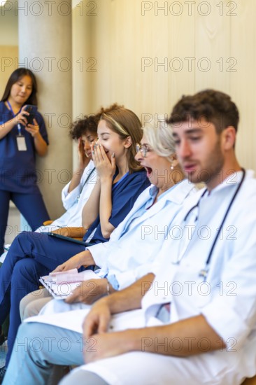 Exhausted doctors and nurses yawning while sitting in a hospital hallway, waiting for their next shift or assignment