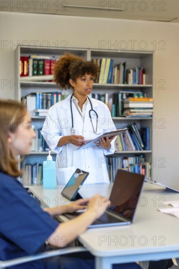 Doctors and nurses using laptops and tablets during a medical briefing, discussing patient charts and reports with a senior doctor holding a clipboard