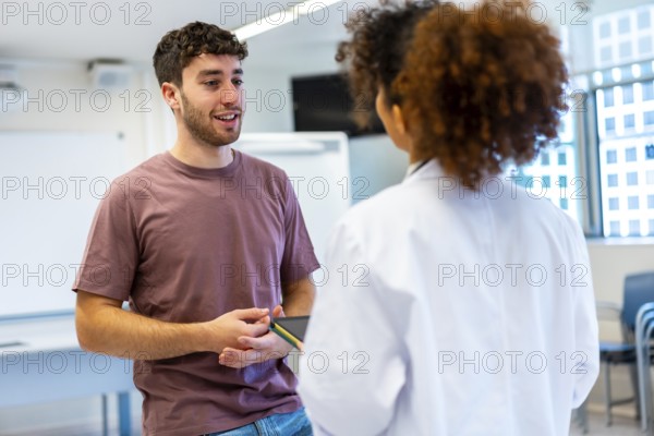Young man holding a tablet, engaging in a conversation with a doctor inside a hospital room, discussing health and treatment options
