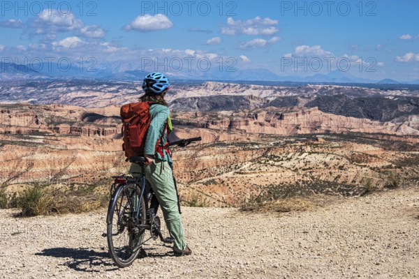 Woman on a bicycle looks over the desert, viewpoint, Gorafe Desert, UNESCO Granada Geopark, Granada province, Andalusia, Spain