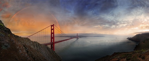 Panoramic view of the Golden Gate Bridge with a rainbow at sunset and orange-glowing storm clouds, San Francisco, California, United States