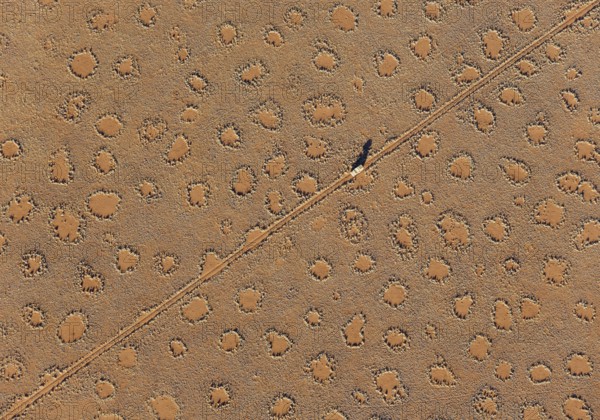 A vehicle of the balloon ground crew crosses a sandy plain with so-called Fairy Circles at the edge of the Namib Desert, photographed from a hot-air balloon, NamibRand Nature Reserve, Namibia
