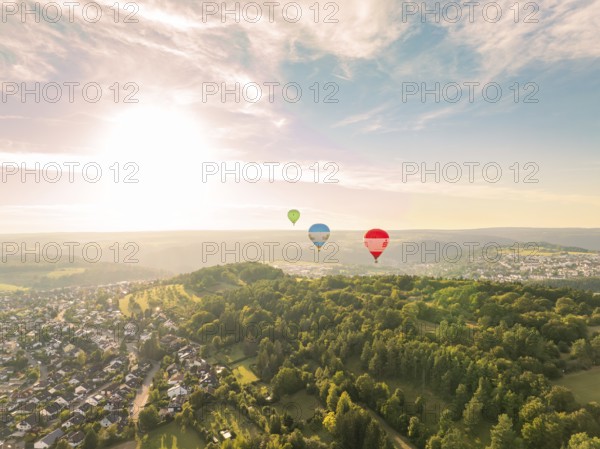 Hot air balloons float over a hilly and wooded landscape at sunset, Calw, Black Forest, Germany