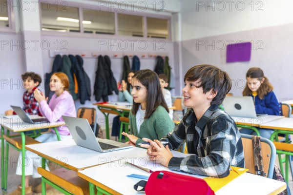 Elementary school students listening to the teacher and participating in the lesson using laptops in a modern classroom