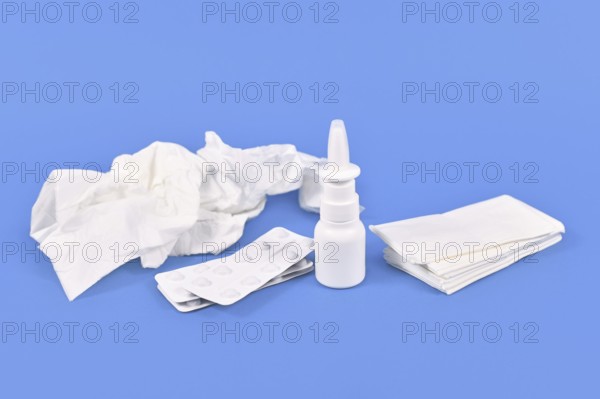 Nasal spray bottle, medicine pills and used tissues used during common cold on blue background