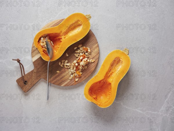 Remove the seeds from a raw butternut squash cut in half using a metal spoon. Cooking techniques and preparation of fresh vegetable ingredients