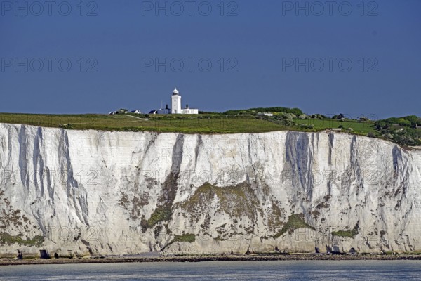 Chalk cliffs with small lighthouse on green grass under blue sky, Dover, Kent, England, Great Britain