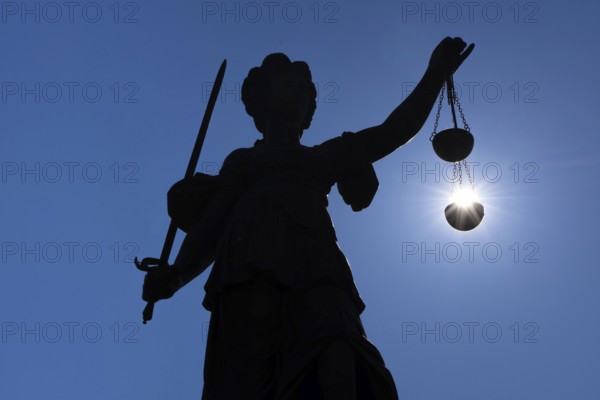 The silhouette of the Justitia statue on the Römerberg in Frankfurt am Main is silhouetted against the sun. It looks as if the sun is lying in her scales of justice, Frankfurt am Main, Hesse, Germany