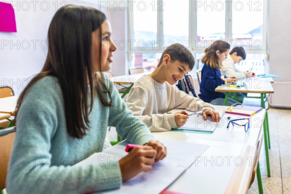 Smiling elementary school students writing on their notebooks during class, learning and education concept