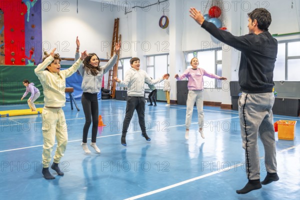 Students and teacher performing jumping jacks during physical education class in school gymnasium, promoting health, fitness, and teamwork