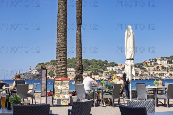 People sitting on a restaurant by the sea at a coast village at a tourist resort, Port de Sóller, Mallorca, Spain
