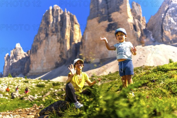 Mother and son waving while hiking on a sunny summer day near the tre cime di lavaredo, a symbol of the dolomites, a unesco world heritage site