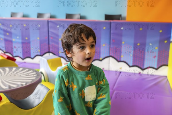 Young boy expressing amazement while playing in a colorful and stimulating indoor playground, featuring soft mats and various play structures