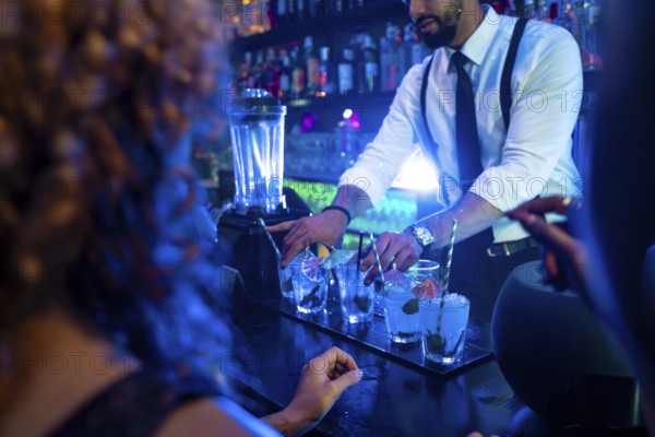 Professional bartender preparing cocktails at bar counter in nightclub, using fresh ingredients and garnishes