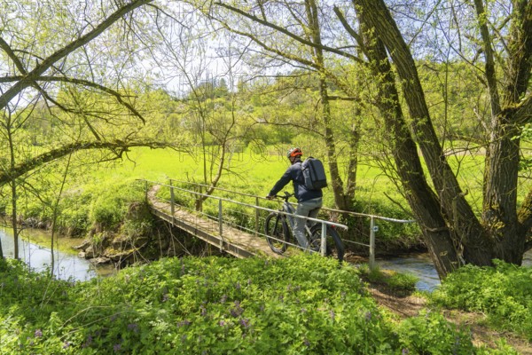 A cyclist enjoys the spring landscape while crossing a bridge in the countryside, Gechingen, district of Calw, Germany
