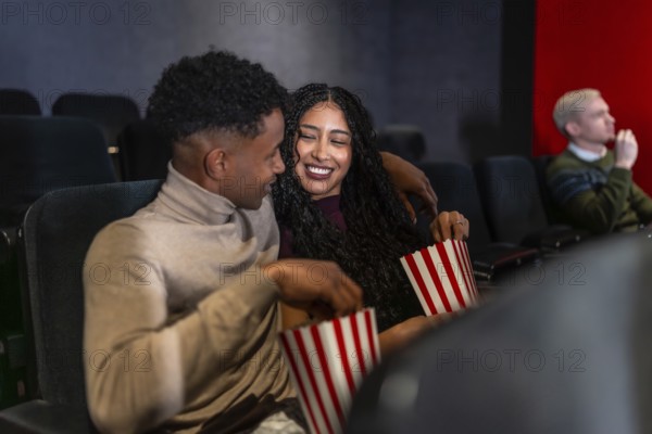 Happy couple enjoying a film in a cozy movie theater, sharing popcorn and laughing together, creating joyful memories on their night out