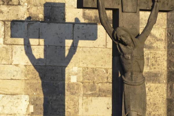 Stone cross with shadow cast at sunrise, cathedral cemetery near Cologne Cathedral, Cologne, North Rhine-Westphalia, Germany