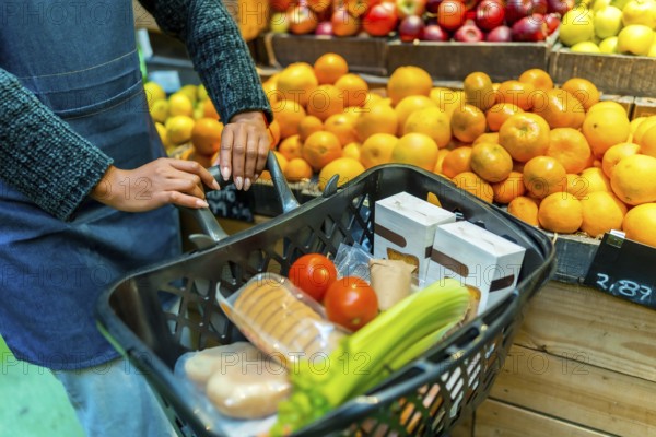 Supermarket employee pushing a shopping cart full of fresh produce, packaged goods, and vegetables in a health food store