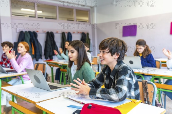 Elementary school students participating in an interactive lesson, raising hands and using laptops in a modern classroom