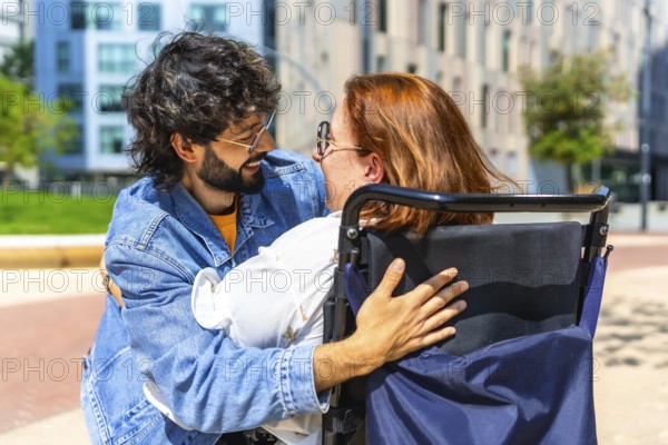 Smiling man hugging a happy woman sitting in a wheelchair in a city park, enjoying a sunny day together