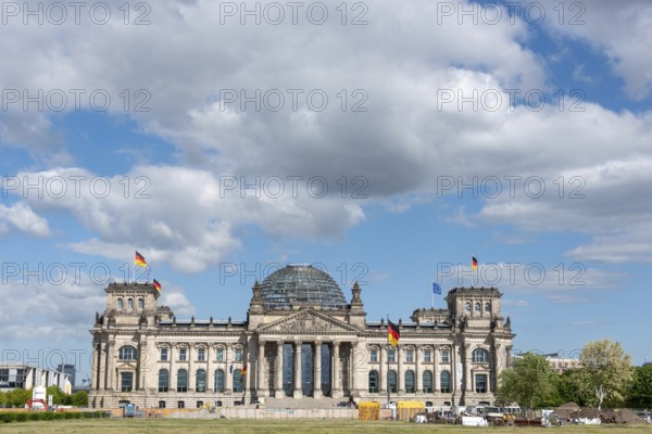 Front view of the Reichstag under a cloudy sky with waving flags, Berlin, Germany