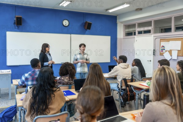Male high school student giving a presentation in front of his diverse classmates and teacher in a modern classroom