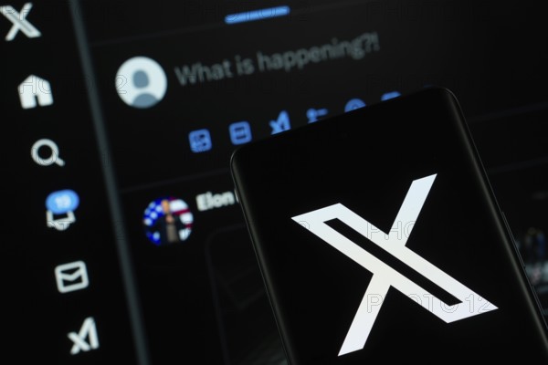 X (twitter) logo is seen on a smartphone, with the bluesky website visible on a computer screen in the background