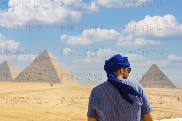 A young tourist wearing blue turban and sunglasses enjoying the Pyramids of Giza, the oldest Funerary monument in the world. In the city of Cairo, Egypt