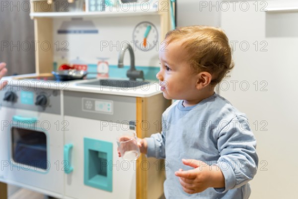 Curious toddler holding a glass while playing with toy kitchen set, exploring and learning through imaginative play